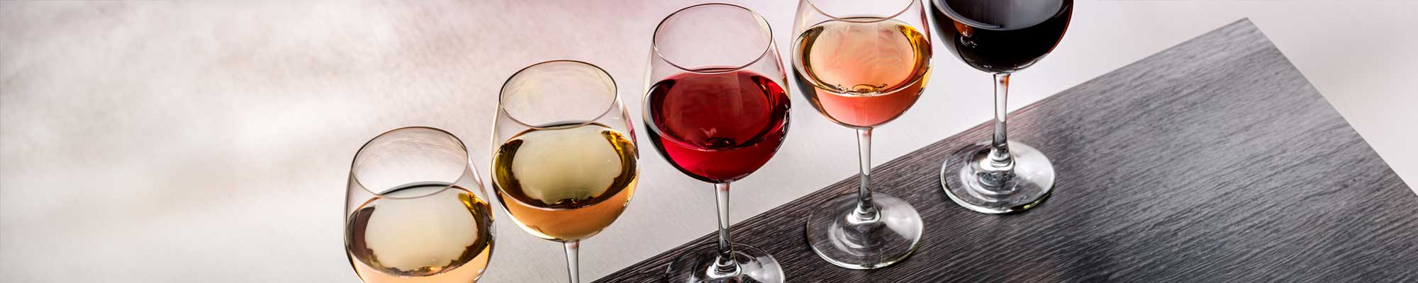 Gefüllte Weingläser in Reihe aufgestellt mit Weißwein, Rotwein und Roséwein