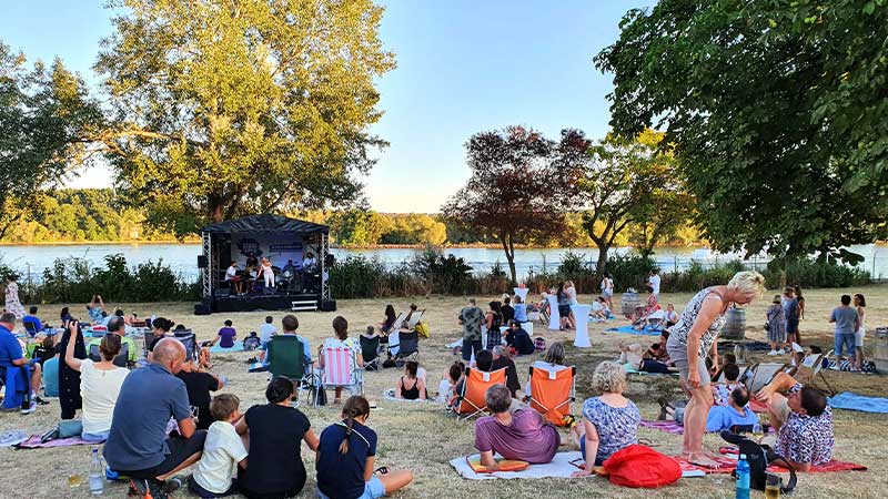 Menschen auf Wiese bei Veranstaltung Sound of Eltville im Freibad der Stadt Eltville mit Konzertbühne am Rhein
