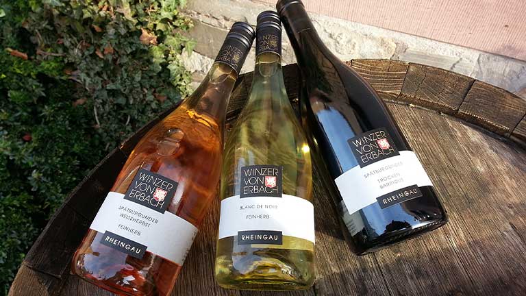Drei liegende Winzer von Erbach Roséwein, Weißwein und Rotwein Flaschen auf Holzfass vor der Winzergenossenschaft